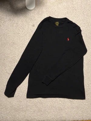 Svart långärmad t-shirt från Polo Ralph Lauren - Säljer en stilren svart långärmad tröja från Ralph Lauren. Klassisk och tidlös modell som passar både till vardag och mer uppklädda tillfällen. Mjuk och skön kvalitet med snygg passform.  🔹 Märke: Ralph Lauren 🔹 Färg: Svart 🔹 Modell: Långärmad tröja 🔹 Skick: Mycket bra skick, sparsamt använd 🔹 Storlek: L/G(14-16) 160 (passar även XS)  Inga fläckar eller hål. Kommer från rök- och djurfritt hem. Skickas snabbt 📦 Hör gärna av dig vid frågor!