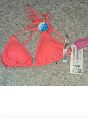 Bikiniöverdel - Säljer en snygg korallrosa bikiniöverdel i trekantsmodell. Den har ribbad struktur och knyt i nacken och ryggen för justerbar passform. Perfekt för strandhäng och sommarvibes!