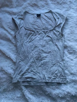 Ljusgrå ärmlös linnetopp - Säljer en enkel och stilren ljusgrå linnetopp med fyrkantig ringning och ärmlös design. Perfekt att matcha med jeans eller kjol för en clean look. Materialet känns mjukt och lätt mot huden. Den är bara skrynklig för det har varit vikt länge i min garderob