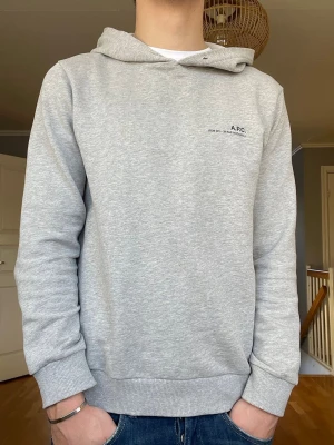 A.P.C grå hoodie – minimalistisk & stilren - Snygg hoodie från A.P.C i klassisk ljusgrå färg. (Snören medkommer såklart) Väldigt fint skick, iprincip ny skick. Mjuk och skön kvalitet, perfekt för både vardag och clean outfits. Inga fläckar, hål eller slitage. Storlek M/S. Skick 9/10. Hör av er vid fler funderingar!🤝
