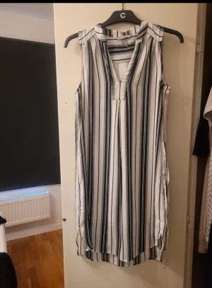 Randig ärmlös klänning från H&M - Snygg ärmlös kortklänning från H&M i storlek 34. Klänningen har svartvita vertikala ränder och en v-ringad hals. Tillverkad i ett lätt och skönt material som passar 