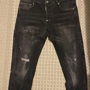 Svarta skinny jeans från Dsquared2 - Svarta jeans från Dsquared2 med slitna detaljer och snygga rippade partier på benen. Modellen är skinny med fem fickor och klassisk knappgylf. Jeansen har en cool Dsquared2-patch baktill och är tillverkade i stretchig denim för skön passform.