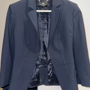 Mörkblå kostym från Elisabetta Franchi - Snygg mörkblå kostym från Elisabetta Franchi med figursydd kavaj och matchande byxor. Kavajen har klassisk krage och markerade sömmar, byxorna har guldiga detaljer vid fickorna och bakfickor med guldfärgad platta. Perfekt för dig som gillar stilrena och exklusiva plagg.övriga delen har storlek 40 och nedre delen har 42 priset kan diskuteras 