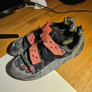 La Sportiva klätterskor svart/röd - Säljer ett par La Sportiva klätterskor i svart och rött med två breda kardborreband. Perfekt för bouldering eller sportklättring. Använda <10 gånger, storlek 45