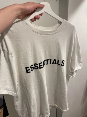  Essentials t-shirt  - Vit t-shirt från Essentials med svart tryck på bröstet och liten Essentials-logga i nacken. Modellen är loose fit med rund hals och korta ärmar. Materialet är mjuk bomull.