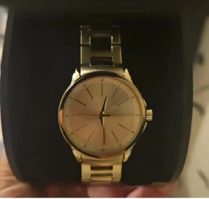 Guldfärgad klocka från Armani Exchange - Stilren guldfärgad klocka från Armani Exchange med metallarmband och minimalistisk urtavla. Klockan har en rund form, tunna indexmarkeringar och tre visare. Perfekt för dig som gillar klassisk och elegant design.