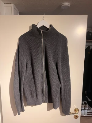 Mörkgrå stickad kofta från East West - Mörkgrå stickad kofta med zip hela vägen, står XL på bilden men den sitter som en M/L. Passar bra med skjorta under.