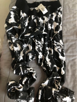 Svarta och vita mönstrade mjukisbyxor - Säljer ett par mjukisbyxor från H&M med svart och vit abstrakt mönster. Byxorna har bred resår i midjan och är gjorda i mjukt bomullsmaterial. Perfekta för chill dagar och har en riktigt cool look.