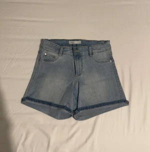 Blå jeansshorts från H&M - Snygga blå jeansshorts från H&M med klassisk femficksdesign och uppvikta benslut. Shortsen har normal passform och är perfekta för varma dagar. Tillverkade i mjuk bomull med knapp och dragkedja framtill.