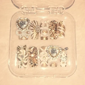 Fina naglar - Vita och Guldiga naglar.	Tumme: 1,5cm. Pekfinger: 1cm. Långfinger: 1,1cm. Ringfinger: 1,1cm. Lilfinger: 9mm. Kommer med nagel fil och nageltejp men rekommenderar nagellim. Perfekt för det nya året. Handgjorda, Lyxiga och lockar in massa komplimanger (jag har gjort andra och fått massa komplimanger trust me). Festliga, gulliga, Y2K, gyaru. 