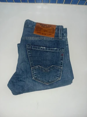 Replay Waitom jeans  - Snygga Replay Waitom jeans i klassisk blå tvätt med regular fit. Jeansen har raka ben, fem fickor och coola detaljer på bakfickorna. Midja 40cm, längd 104cm. JAG SKICKAR EJ FLER BILDER NÄR JAG BÄR JEANSEN! för storleksguide hänvisar jag till måtten och för bättre inblick i passformen rekommenderar jag att googla på modellnamnet. kolla måtten noggrant :) 73