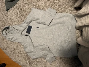 Grå hoodie från Polo Ralph Lauren M - Snygg grå hoodie från Polo Ralph Lauren i storlek M. Klassisk design med huva och dragsko, känguruficka framtill och mörkblå broderad logga på bröstet. Mjuk bomullsblandning som är skön att ha på sig. Perfekt för chill dagar.