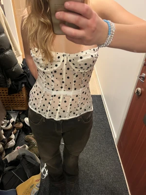 Vit prickig korsett med svarta prickar - Supersnygg vit korsett med svarta prickar och markerade sömmar. Toppen är axelbandslös och har en figurnära passform som framhäver midjan och går att spänna åt i bak. Den är i storlek L men eftersom den går att justera passar den även mindre storlekar. Perfekt för dig som vill sticka ut med en trendig look. 