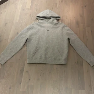Grå hoodie från Axel Arigato(storlek 164/178) - Snygg ljusgrå hoodie från Axel Arigato med minimalistisk svart logga på bröstet. Klassisk modell med huva, känguruficka och långa ärmar. Perfekt för en chill och stilren look. Mjuk insida och relaxed fit.