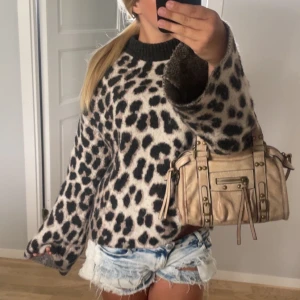 Leopardmönstrad stickad tröja - Säljer en supermjuk och oversized stickad tröja med leopardmönster i svart och beige. Tröjan har breda ärmar och ribbad kant vid halsen. Perfekt för dig som vill sticka ut och hålla dig varm under kyliga dagar.