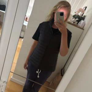 Svart dunväst från Calvin Klein M - Säljer en svart dunväst från Calvin Klein i storlek M. Västen har quiltad design, hög krage och dragkedja framtill. Perfekt att slänga över en hoodie eller t-shirt för en clean och stilren look.