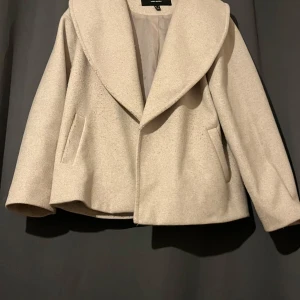 Beige kappa från Vero Moda - Säljer en stilren beige kappa från Vero Moda med bred krage och fickor på sidorna. Jackan har en mjuk ullblandning och är perfekt för höst och vår. Enkel och tidlös design som passar till många outfits.