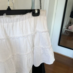 Vit volangkjol med shorts från pull&bears - Supersöt vit kortkjol med volanger och inbyggda shorts. Det finns inga tecken på användning då den är oanvänd. Köptes i Polen och är i storlek M. Pris kan diskuteras