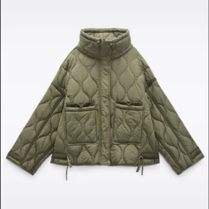 Olivgrön quiltad pufferjacka - Säljer en olivgrön pufferjacka med quiltad design och hög krage. Jackan har två stora fickor framtill med snygga detaljer och dragsko i nederkant. Perfekt för dig som vill ha en cool och trendig look under kyliga dagar.