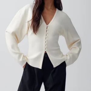 Figursydd topp från Gina Tricot - Superfin vit kofta från Gina Tricot med v-ringning och snygga klädda knappar framtill. Koftan är i mjukt stickat material och har långärmad passform. Aldrig använd. 