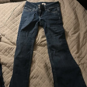 Blå bootcut jeans med broderade fickor - Snygga blå jeans med bootcut passform och coola broderade detaljer på bakfickorna. Klassisk femficksmodell med dubbla knappar och dragkedja framtill. Jeansen har kontrastsömmar och är tillverkade i ett mjukt denimtyg.