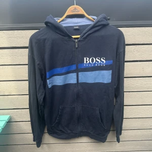 Blå Hugo Boss Hoodie - Blå Hugo Boss hoodie i storlek M. Denna säljs inte längre och är därför ganska sällsynt. Skicket är fint, skulle ge den 8/10. Tveka inte på att fråga om du har några frågor 💯