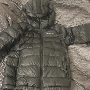 Svart dunjacka Peak Performance - Svart dunjacka från Peak Performance med huva och dragkedja framtill. Jackan har två sidofickor med dragkedja och en bred rem på ryggen för enkel bäring. Puffig design och diskret logga på bröstet och ärmen. Perfekt för kalla dagar. Köpt för 2900 säljer för 1600 pris kan diskuteras.