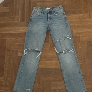Ljusa ripped jeans från Zara - Säljer ett par ljusblå jeans från Zara med raka ben och stora slitningar över knäna. Klassisk femficksmodell med hög midja och råa kanter. Perfekta för en avslappnad och trendig look. Super trendiga 