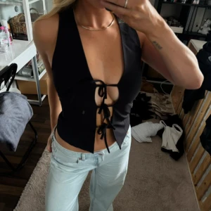 Svart topp med snörning från Zara - Säljer en svart korsett-topp med djup v-ringning och snygg snörning framtill. Toppen är ärmlös och har en croppad passform som ger en edgy look. Perfekt att styla med jeans eller kjol för en trendig outfit.