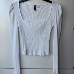 Vit ribbad långärmad topp H&M Divided - Säljer en vit ribbad långärmad topp från H&M Divided. Toppen har fyrkantig ringning, lätt puffade axlar och croppad passform. Perfekt att styla med jeans eller kjol.