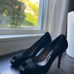 Svarta mockapumps med öppen tå - Snygga svarta pumps från philosophy blues original i mocka med öppen tå och hög klack. Skorna har en elegant design med korslagda detaljer framtill och en klassisk siluett som passar perfekt till en dressad look.