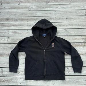 Svart hoodie från Polo Ralph Lauren - Svart hoodie från Polo Ralph Lauren med dragkedja och huva. På bröstet finns den ikoniska broderade Polo-björnen. Storlek 14-16 vilket motsvarar xs. Skick 8/10 tveka inte på att skriva om ni har några frågor. Pris kan diskuteras🙌