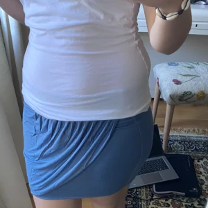 Blå omlott kortkjol - Säljer en blå kortkjol med omlott-detalj och snygg drapering framtill. Kjolen har en tight passform och är perfekt för dig som gillar en enkel men trendig look. Materialet känns mjukt och stretchigt, vilket gör den bekväm att bära hela dagen. Okännt märke. 