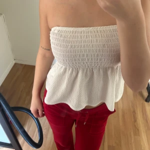 Vit bandeau tubtopp från Gina Tricot - Supersöt vit bandeau tubtopp från Gina Tricot i storlek XS. Toppen är smockad upptill och har en volangig, utsvängd nederdel. Gjord i ett lätt, strukturerat tyg som känns luftigt och perfekt för varma dagar.