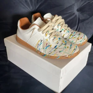 Maison Margiela Paint Splatter - Super snygga Maison Margielas i vitt skinn med färgstänk som gör de unika. Skorna är super sköna och skornas skick är mycket bra skick nästan ny skick. Perfekt för dig som vill sticka ut med en kreativ och trendig look. Boxen tillkommer🤗 Jag tar även emot byten om de skulle vara så💯