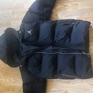 Svart pufferjacka från Jordan - Säljer en svart pufferjacka från Jordan med huva och dragkedjor på sidorna. Jackan har det klassiska Jumpman-loggan på bröstet och är riktigt dunig och varm. Perfekt för kalla dagar och har en clean streetstyle-vibe.