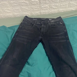 Svarta Replay jeans, midja 31 längd 32 - Säljer ett par svarta Replay jeans med snygga slitningar och klassisk femficksdesign. Jeansen har vita kontrastsömmar och normal passform. Perfekta för dig som gillar stilrena och bekväma jeans med lite edge. Säljer dem pågrund av att jag rensar min garderob. Kostar 1700 nya 