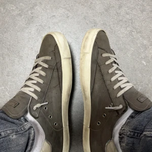 Philippe Model grå sneakers i skinn - Säljer ett par Philippe Model sneakers i grått skinn med vita snören och vit sula. Klassisk låg modell med rund tå och diskret logga på sidan. Snygg kontrast mellan den grå ovandelen och den slitna vita sulan. Perfekta för en avslappnad streetstil, små defekter på hälen av sulan annars är dem väldigt bra skick, det är även en sliten look på skorna så missta inte dem för att dem ser använda ut, skriv om ni har mer frågor!