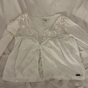 Vit blus med spets från Monrow - Supersöt vit blus från Monrow med långa ärmar och v-ringning. Överdelen har detaljerad virkad spets och små knappar framtill. Blusen har en luftig och flowy passform, .