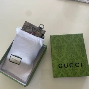 Gucci plånbok med orm och logomönster - Snygg plånbok från Gucci med klassiskt GG-monogram och en cool röd och vit orm på framsidan. Plånboken har dragkedja och en grön-röd handledsrem. Perfekt för kort och småsaker, och levereras i originalask och dustbag.