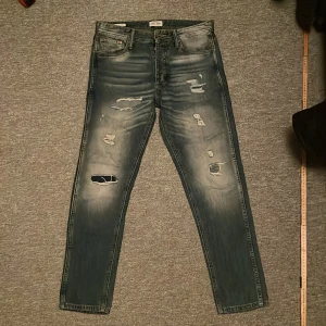 Blå slitna jeans från Jack & Jones - Säljer ett par blå jeans från Jack & Jones i modellen Anti Fit/erik. Feta slitningar med lite tvätt. Inga defekter, förutom slitningar vid tillverkning. Pm vid frågor och funderingar!