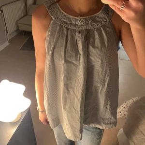 Randig ärmlös blus från French Connection - Säljer en snygg blus från French Connection i vitt och grått med tunna ränder. 