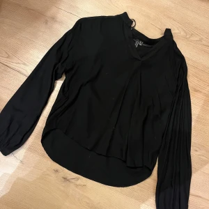 Svart blus med v-ringning Vero Moda - Svart blus från Vero Moda i storlek S. Blusen har v-ringad hals, långärmade ärmar med lätt puff och en något längre bakdel för cool siluett. Materialet är mjukt och lätt, perfekt för att styla med jeans eller kjol.