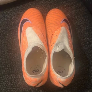 Nike Phantom orange fotbollsskor - Säljer ett par grymt snygga Nike Phantom fotbollsskor i orange med svarta och lila detaljer. Skorna har en strumpliknande vit ovandel och är designade för att ge bra känsla och kontroll på planen. Perfekt för dig som vill sticka ut med färg och stil.