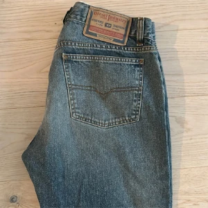 Diesel jeans straight fit blå 34 - Snygga blå jeans från Diesel i klassisk straight fit med fem fickor och knappgylf. Jeansen har en cool vintage-look med diskreta slitningar och är tillverkade i robust denim. Passar dig som gillar tidlös stil och italiensk kvalitet.
