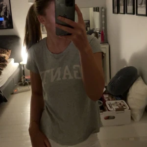 Grå t-shirt från Gant - Säljer en grå t-shirt från Gant med klassisk rund halsringning och vit logga framtill. T-shirten har korta ärmar och är i mjuk bomull, perfekt för en chill och stilren look. Super skön och verkligen tråkigt att den inte kommer till användning 