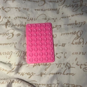 Mobil fäste - Bilderna visar ett rosa mobil fäste i silikon. Produkten är i gott skick utan synliga defekter eller slitage. Perfekt om du vill sätta din mobil på spegeln eller glas