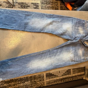 Blå jeans från Raoshi, storlek 33 - Säljer ett par snygga blå jeans från Raoshi i storlek 33. Jeansen har klassisk femficksdesign, ljusa slitningar och raka ben. Materialet är bomull och de har en cool detalj på bakfickorna med mörkare sömmar. Perfekt för dig som gillar en avslappnad stil.