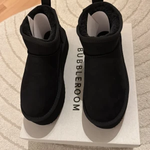 Svarta Bernice Mini platform boots - Svarta Bernice Mini platform boots från Bubbleroom i storlek 39. Boots med plattformsula och rund tå, fodrade med mjukt material för extra komfort. Yttermaterialet är mocka och insidan är fluffig, perfekt för kalla dagar. Snygg och chunky look med dragflik bak.