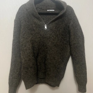 Mörkgrå stickad tröja med half zip Zara - Mysig mörkgrå stickad tröja från Zara i storlek M. Tröjan har ribbad struktur, lång ärm och en snygg half zip-dragkedja vid halsen som ger en cool look. Perfekt för kyliga dagar och enkel att matcha med jeans eller cargo.
